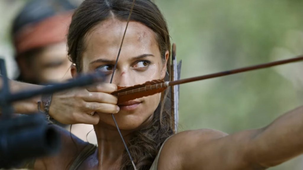 Alicia Vikander segura uma fecha armada em um arco, apontando para a frente. Alicia Vikander vive Lara Croft na adaptação do game para o cinema..